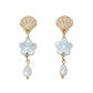 Mellow Monkey scallop shell earrings featuring light blue ceramic flowers and white pearl drops in gold-tone metal.