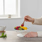 Mellow Monkey decorative white scalloped bowl with two blue ceramic birds on rim, filled with fruit.
