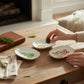 Mellow Monkey stoneware scalloped dishes with festive holiday illustrations and gold electroplated rims on a table.