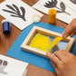 Mellow Monkey screen printing kit with wooden frame, yellow paint, squeegee, and stencils on a wooden table.