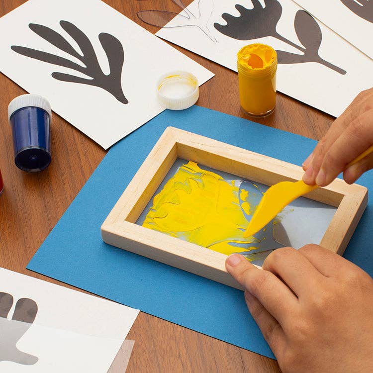 Mellow Monkey screen printing kit with wooden frame, yellow paint, squeegee, and stencils on a wooden table.