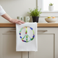 Mellow Monkey white cotton flour sack towel featuring a colorful sea glass peace sign design hanging in a kitchen.