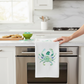 Mellow Monkey white cotton flour sack towel featuring a festive sea glass Santa crab design hanging on an oven handle