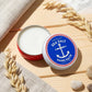 Mellow Monkey Swedish Dream Sea Salt Hand Salve in a round red tin with an anchor logo on a wooden surface.
