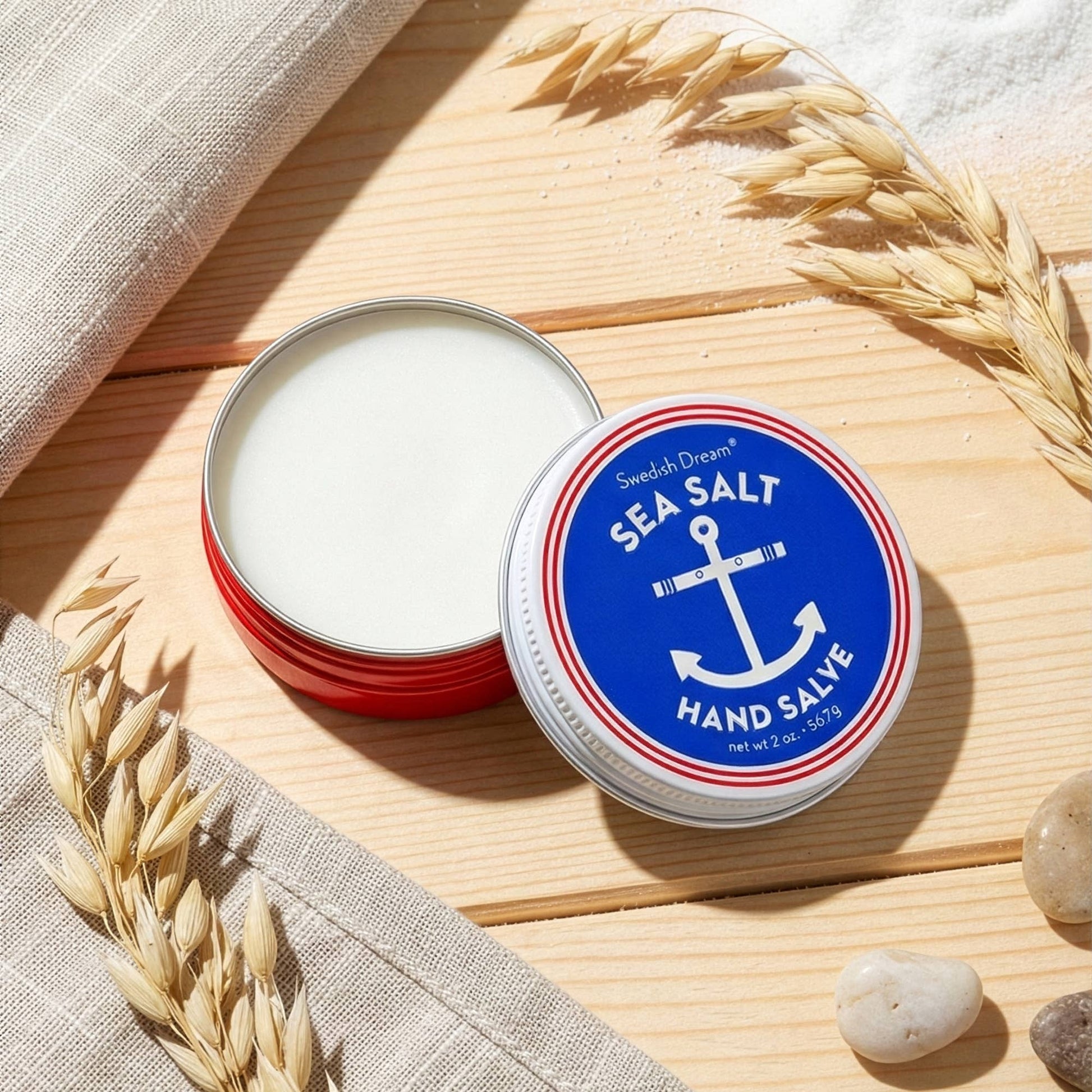 Mellow Monkey Swedish Dream Sea Salt Hand Salve in a round red tin with an anchor logo on a wooden surface.