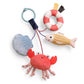 Mellow Monkey Itzy Travel Charms Seaside baby toy featuring a soft plush crab, fish, shell, and lifebuoy on a clip.