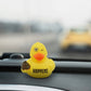 Mellow Monkey Shit Happens rubber duck with a winking expression, sitting on a car dashboard.