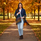 Mellow Monkey Sidney Fringe Wrap in midnight plaid with tassel accents worn by a woman in an autumn park setting.