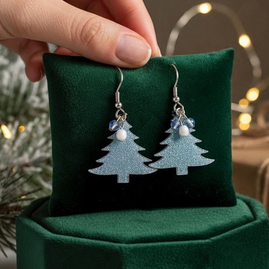 Mellow Monkey silver glittery Christmas tree earrings with surgical steel wires displayed on a green velvet cushion.
