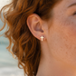 Mellow Monkey minimalist silver cross stud earring worn on a woman with red hair against a blurred beach background