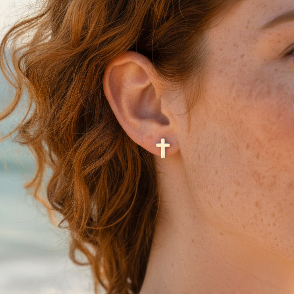 Mellow Monkey minimalist silver cross stud earring worn on a woman with red hair against a blurred beach background