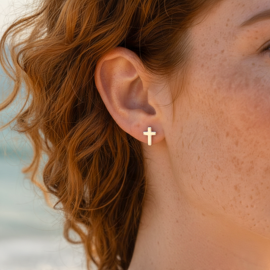 Mellow Monkey minimalist silver cross stud earring worn on a woman with red hair against a blurred beach background