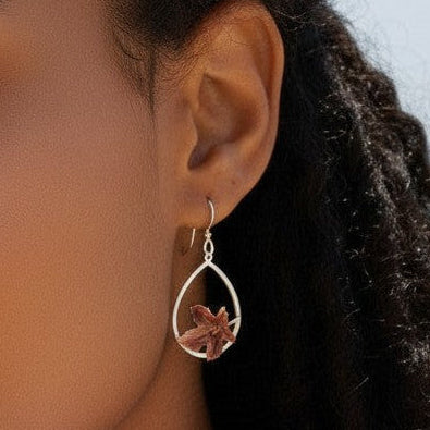 Mellow Monkey silver hoop earrings with a delicate leaf charm worn by a woman at the beach.