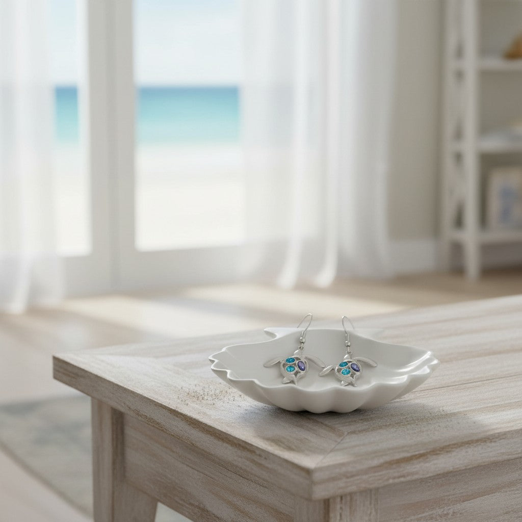 Mellow Monkey silver turtle earrings with blue crystals resting in a white shell dish on a wooden table.