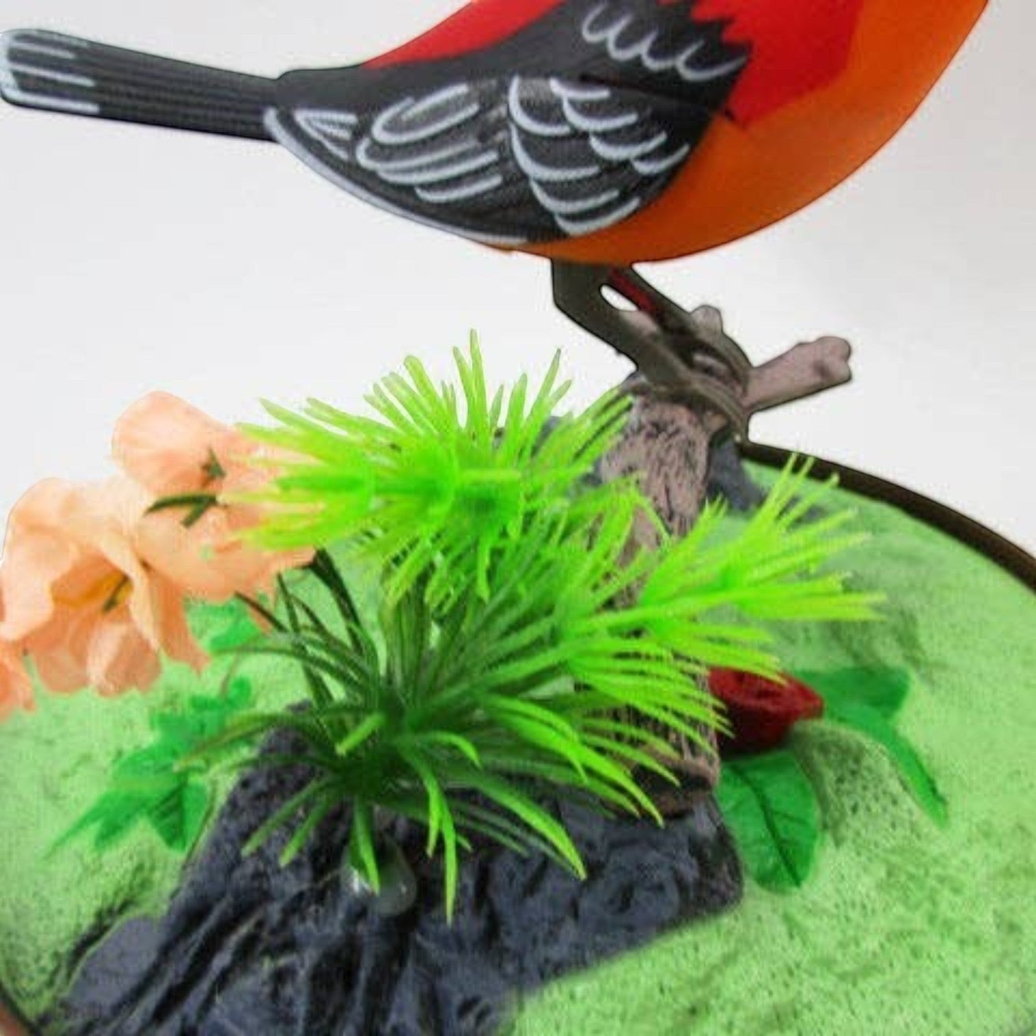 Mellow Monkey sound-activated singing bird toy perched on a branch with artificial flowers and green base
