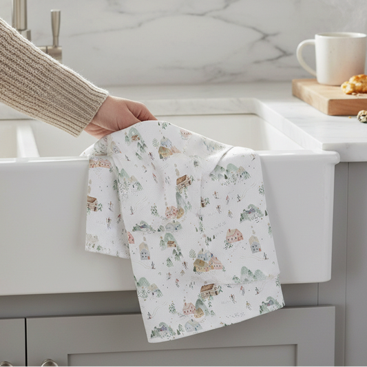 Mellow Monkey waffle dish towel with a colorful ski resort print, held over a white farmhouse kitchen sink.