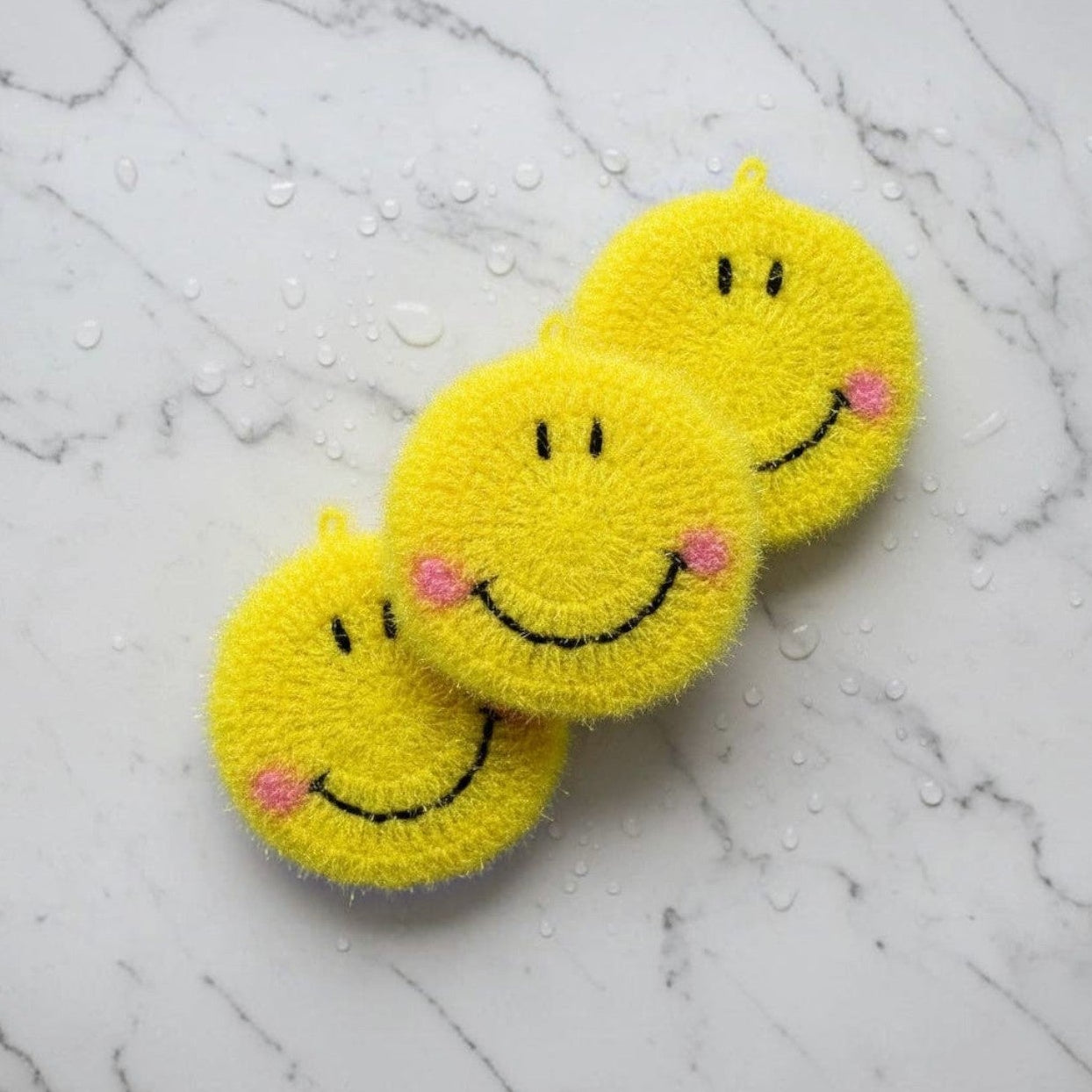 Mellow Monkey Sunny Scrubby Set of three bright yellow smiley face dish scrubbers on a white marble surface