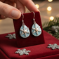 Mellow Monkey silver snowflake teardrop earrings with a central pearl, displayed on a red velvet stand.