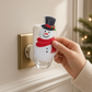 Mellow Monkey snowman fragrance warmer with a red scarf and top hat plugged into a wall outlet for festive decor