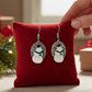 Mellow Monkey handmade silver oval earrings featuring a snowman with a green scarf on a red velvet display cushion.