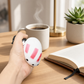 Mellow Monkey Chilly the Snowman squishy toy being squeezed by a hand on a wooden desk with a coffee mug and book.