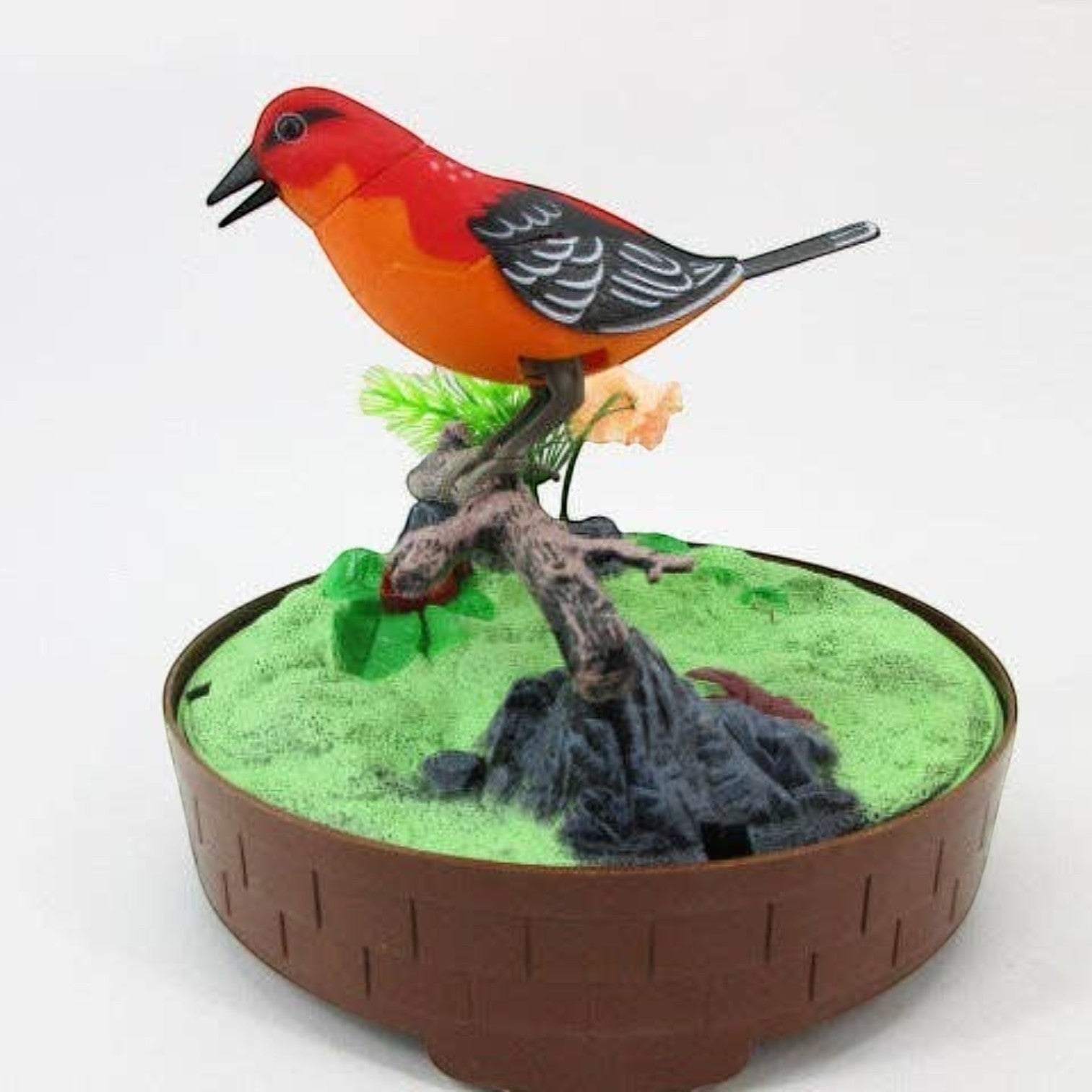 Mellow Monkey sound-activated red singing bird toy perched on a branch inside a decorative cage base