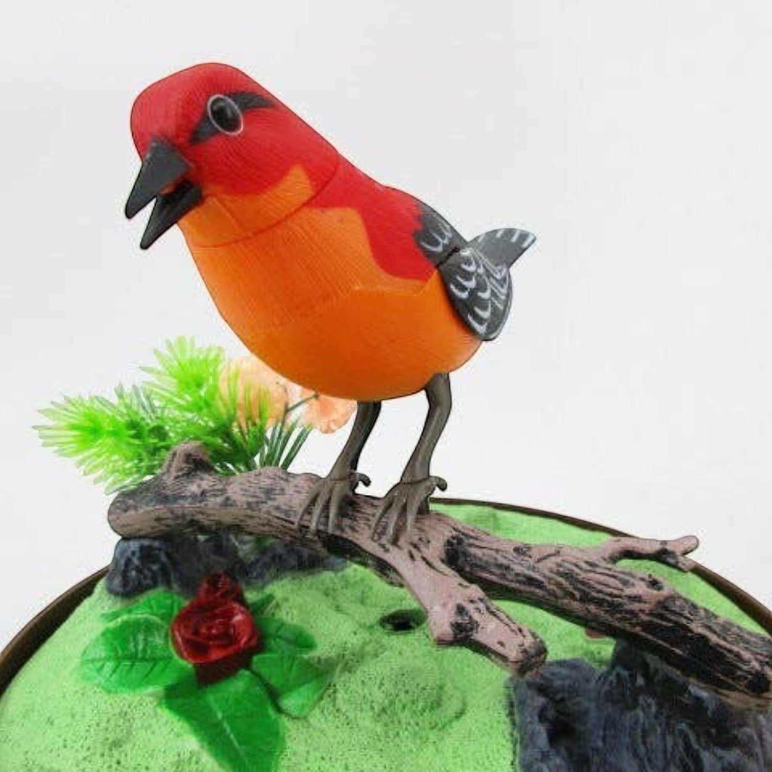 Mellow Monkey sound-activated red and orange toy bird on a branch inside a decorative cage