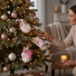 Woman hanging Mellow Monkey Spa Day Mice ornaments on a decorated Christmas tree with rose gold baubles.