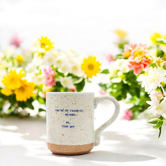 Mellow Monkey handmade ceramic mug with speckles and You're My Favorite Weirdo quote, set against colorful flowers.