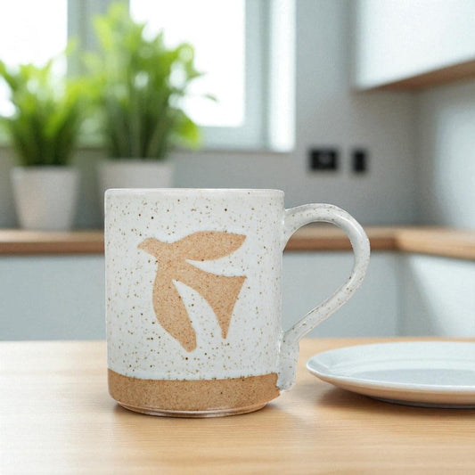 Mellow Monkey speckled stoneware mug featuring a hand-carved bird design on a wooden kitchen table.