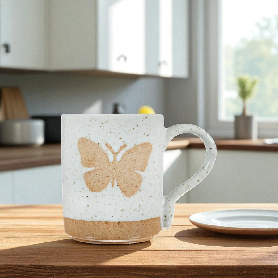 Mellow Monkey speckled stoneware mug featuring a hand-carved butterfly design on a kitchen table.
