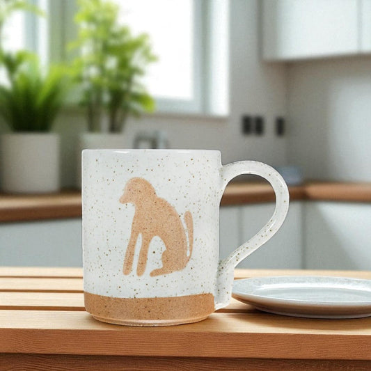 Mellow Monkey speckled stoneware mug featuring a tan dog silhouette on a white background, sitting on a wooden table.