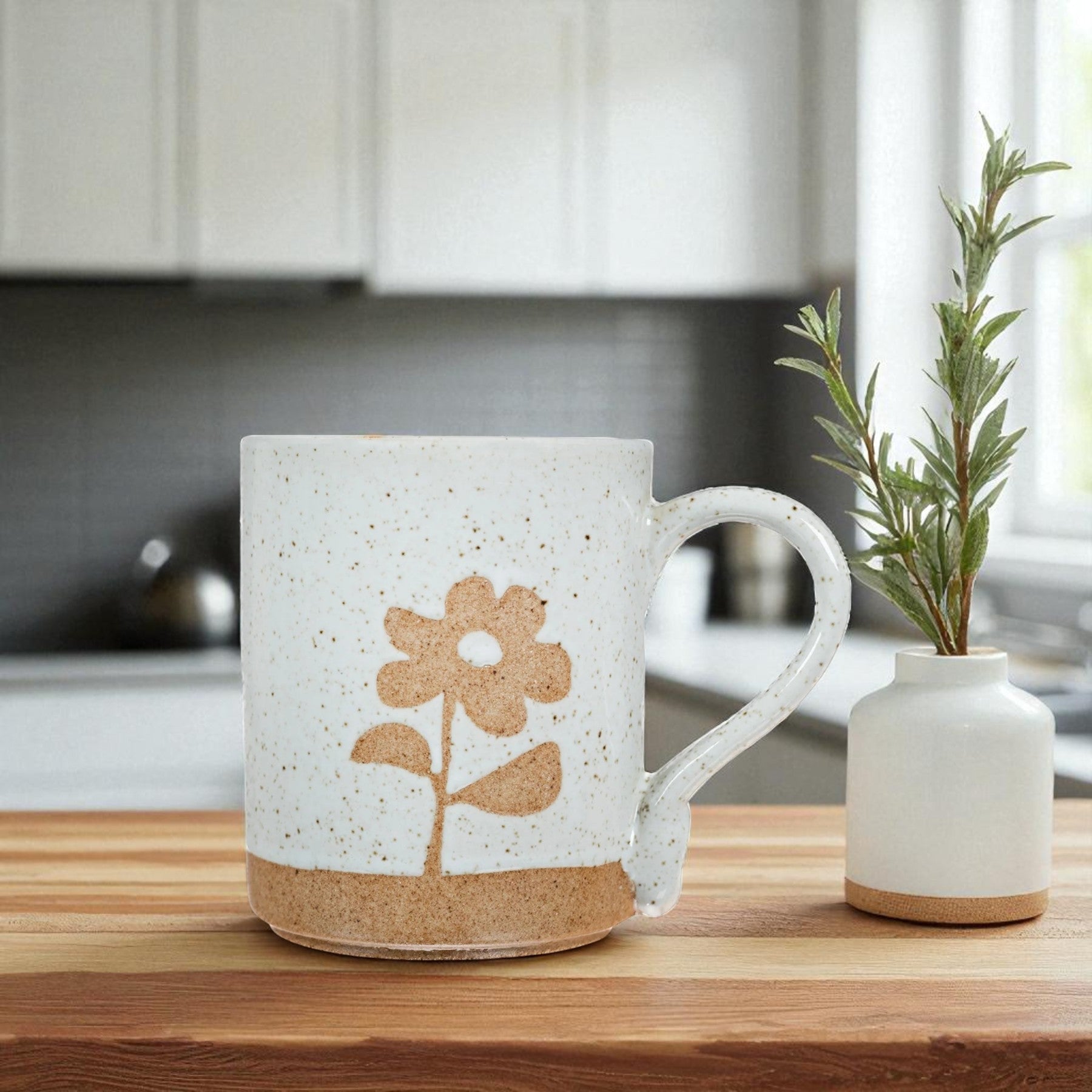 Mellow Monkey speckled stoneware mug featuring a hand-carved flower design on a wooden kitchen table