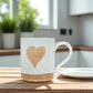 Mellow Monkey speckled stoneware mug featuring a hand-carved heart design on a wooden table in a bright kitchen.
