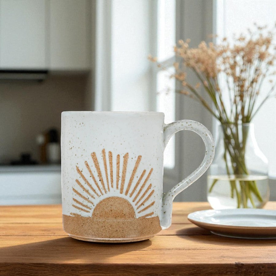 Mellow Monkey speckled stoneware mug featuring a hand-carved sun design on a wooden table in a bright kitchen.