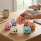 Mellow Monkey 3.25 inch colorful slow-rise squishy dumpling toys with cute faces being squeezed on a wooden desk