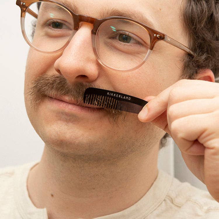Mellow Monkey stainless steel mini mustache comb being used by a man with glasses to groom his facial hair.