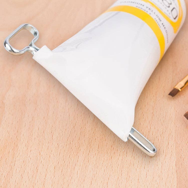 Mellow Monkey stainless steel tube squeeze key used to dispense paint from a tube on a wooden surface