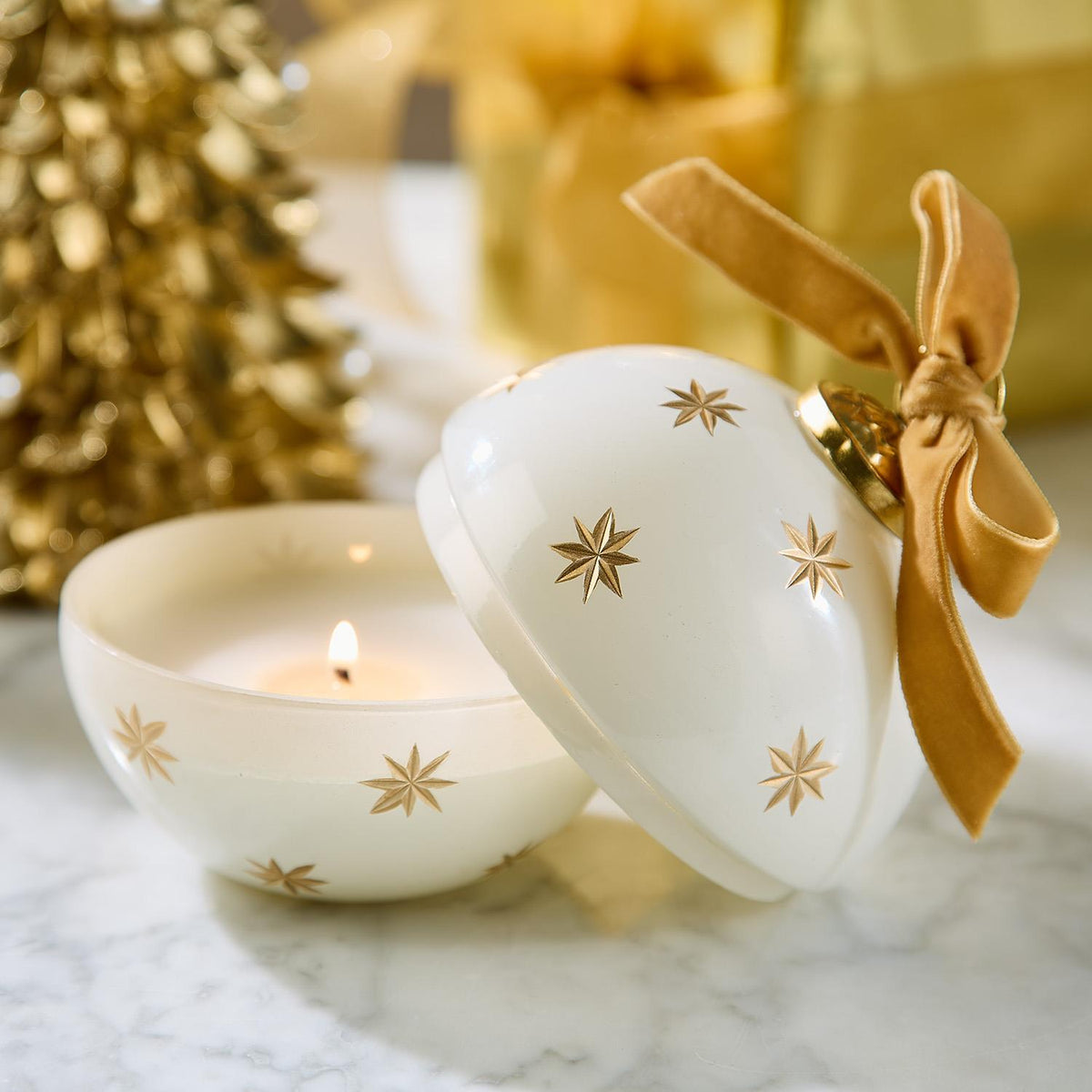 Mellow Monkey star-studded ornament candle in white glass with gold stars and a velvet ribbon on a marble surface