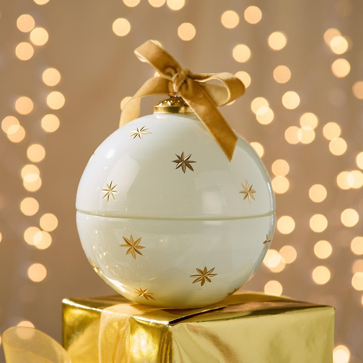 Mellow Monkey star-studded white glass ornament candle with gold stars and a velvet ribbon on a gold gift box.