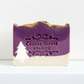 Mellow Monkey Starry Night artisan soap bar with purple and white layers, gold glitter, and a white pine tree design.