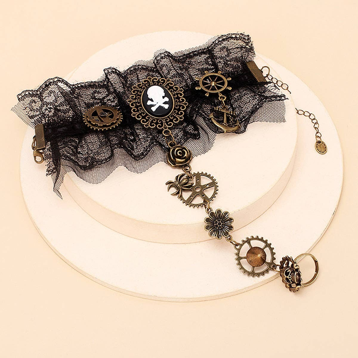 Mellow Monkey steampunk lace hand bracelet with skull cameo, bronze gears, and charms on a beige display stand.