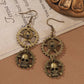 Mellow Monkey steampunk drop earrings featuring bronze-tone gears and skull charms on hook backings.