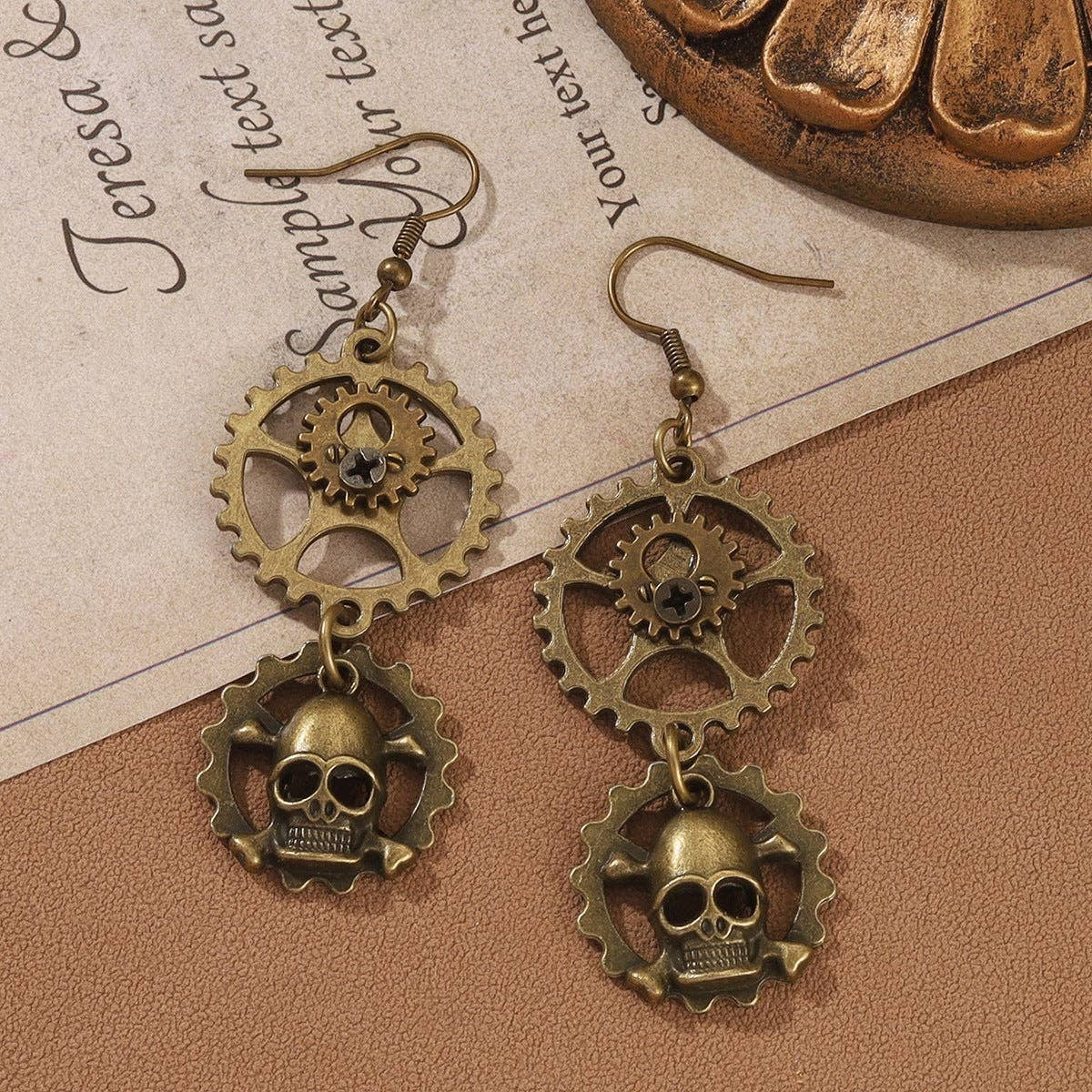 Mellow Monkey steampunk drop earrings featuring bronze-tone gears and skull charms on hook backings.