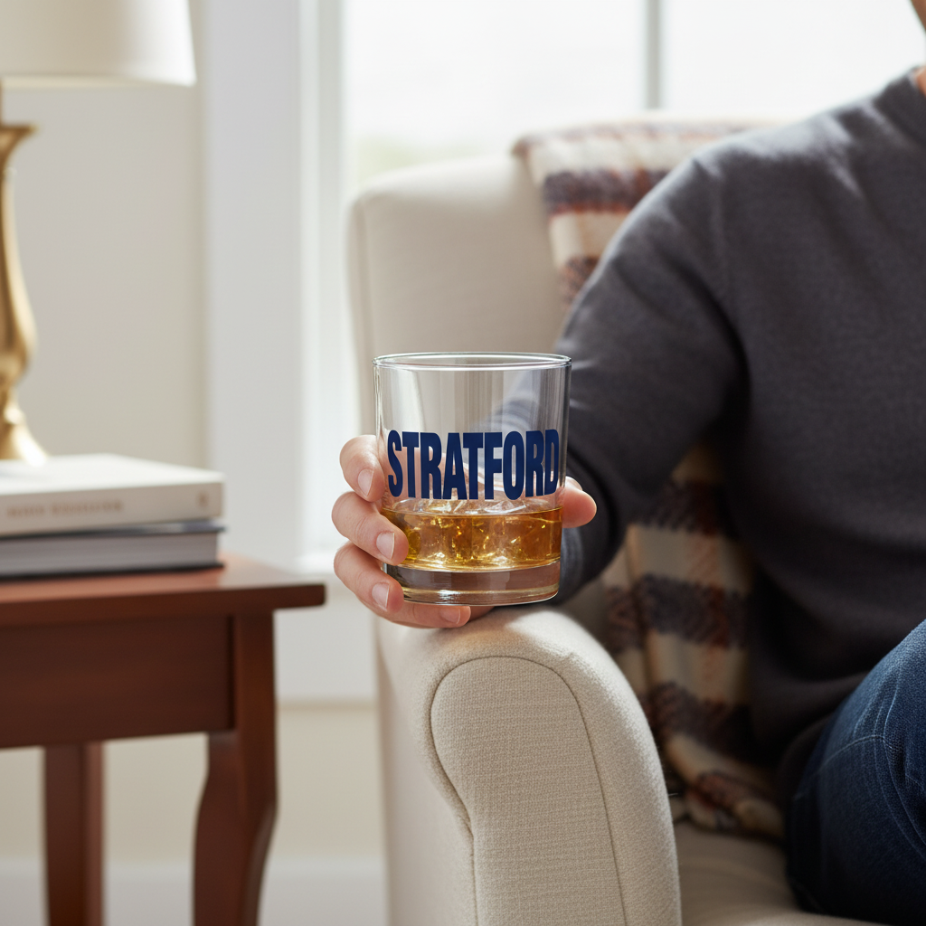 Mellow Monkey Stratford rocks glass filled with whiskey held by a person sitting in a cozy armchair