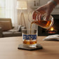 Mellow Monkey Stratford rocks glass filled with whiskey on a wooden table with a cozy fireplace in the background