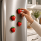 Mellow Monkey set of four hand-painted polyresin strawberry magnets attached to a stainless steel refrigerator door.