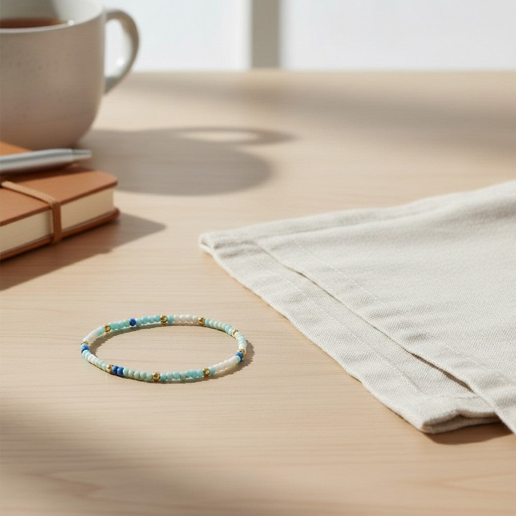 Mellow Monkey stretch seed bead bracelet in blue, mint, and white with 18k gold-plated brass accents on a table.