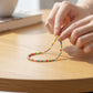 Mellow Monkey stretch seed bead bracelet in aqua, yellow, and red with 18k gold plated brass accents on a table.