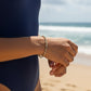 Mellow Monkey stretch seed bead bracelet in taupe, peach, and grey with 18k gold-plated accents worn on a beach.